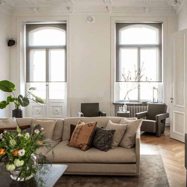 Frihängande rullgardiner i ljusgrått i vardagsrum i sekelskiftesvilla, höga fönster med halvmåneöppning och elegant inredning