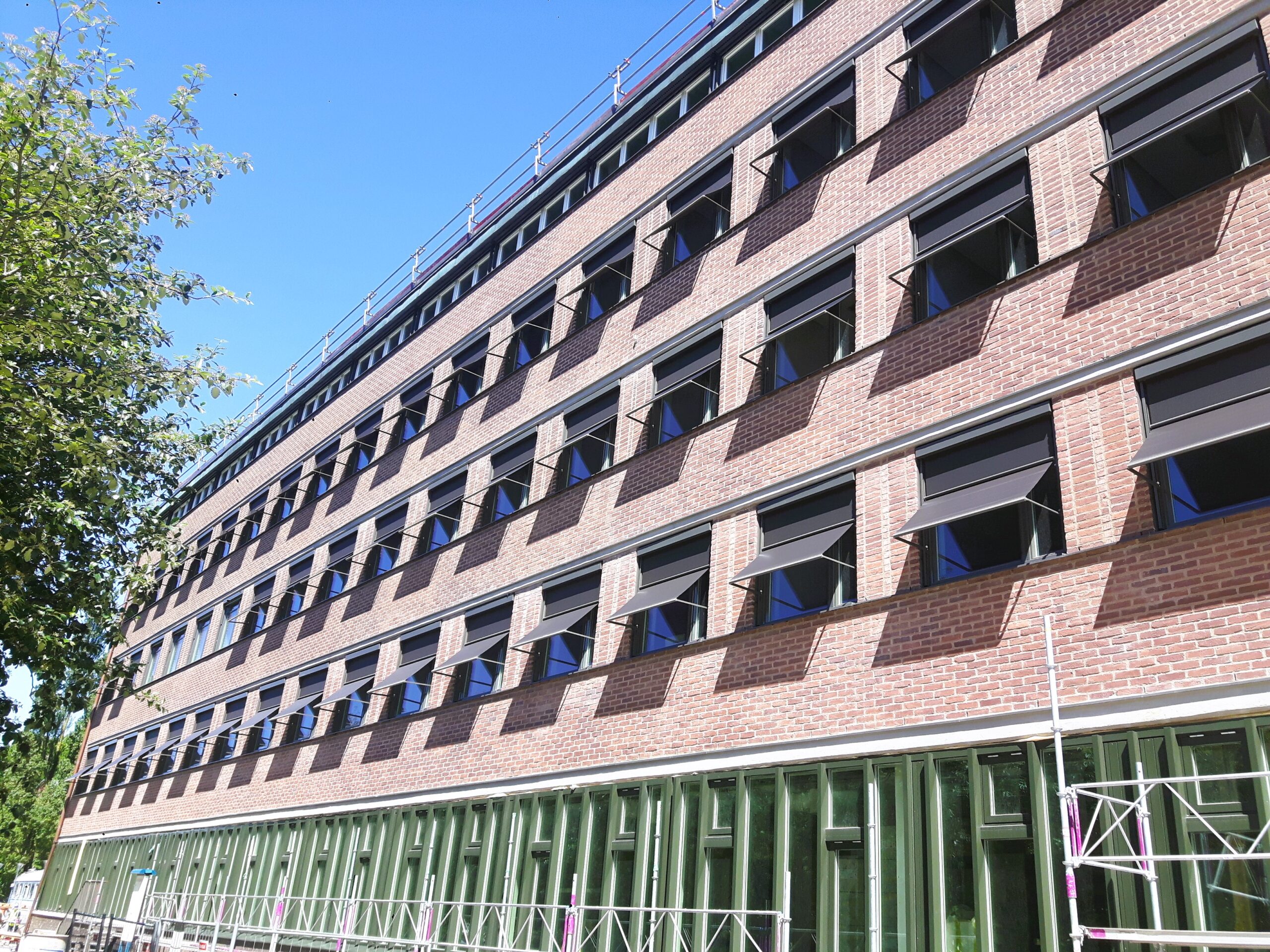 Fasad med svarta utåtstående markisoletter på universitet i tegel, flera etapper med solskydd som skuggar fönster