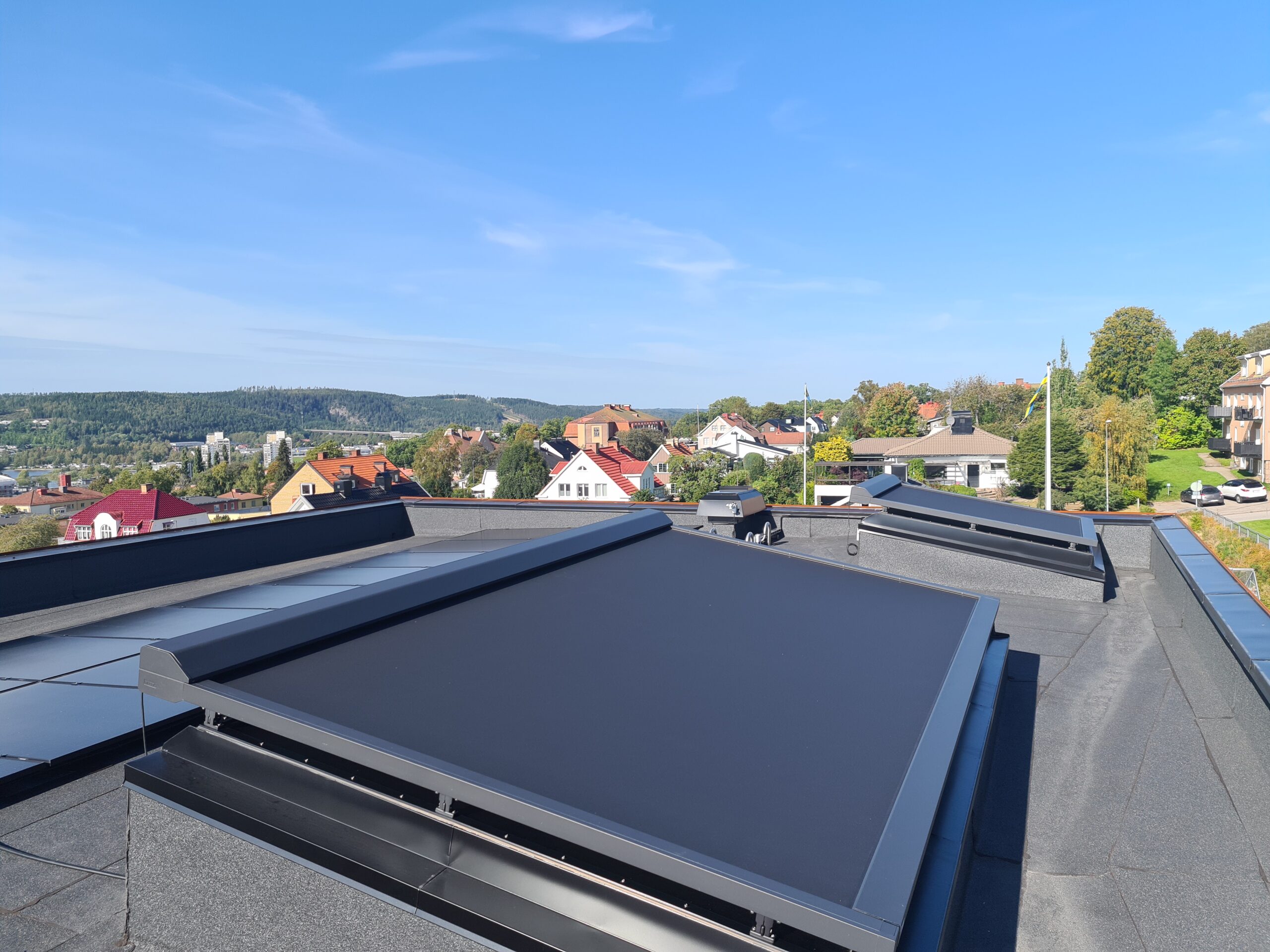 ZIP-screens monterade på takfönster över villatak med vy mot bostadsområde och skog i bakgrunden