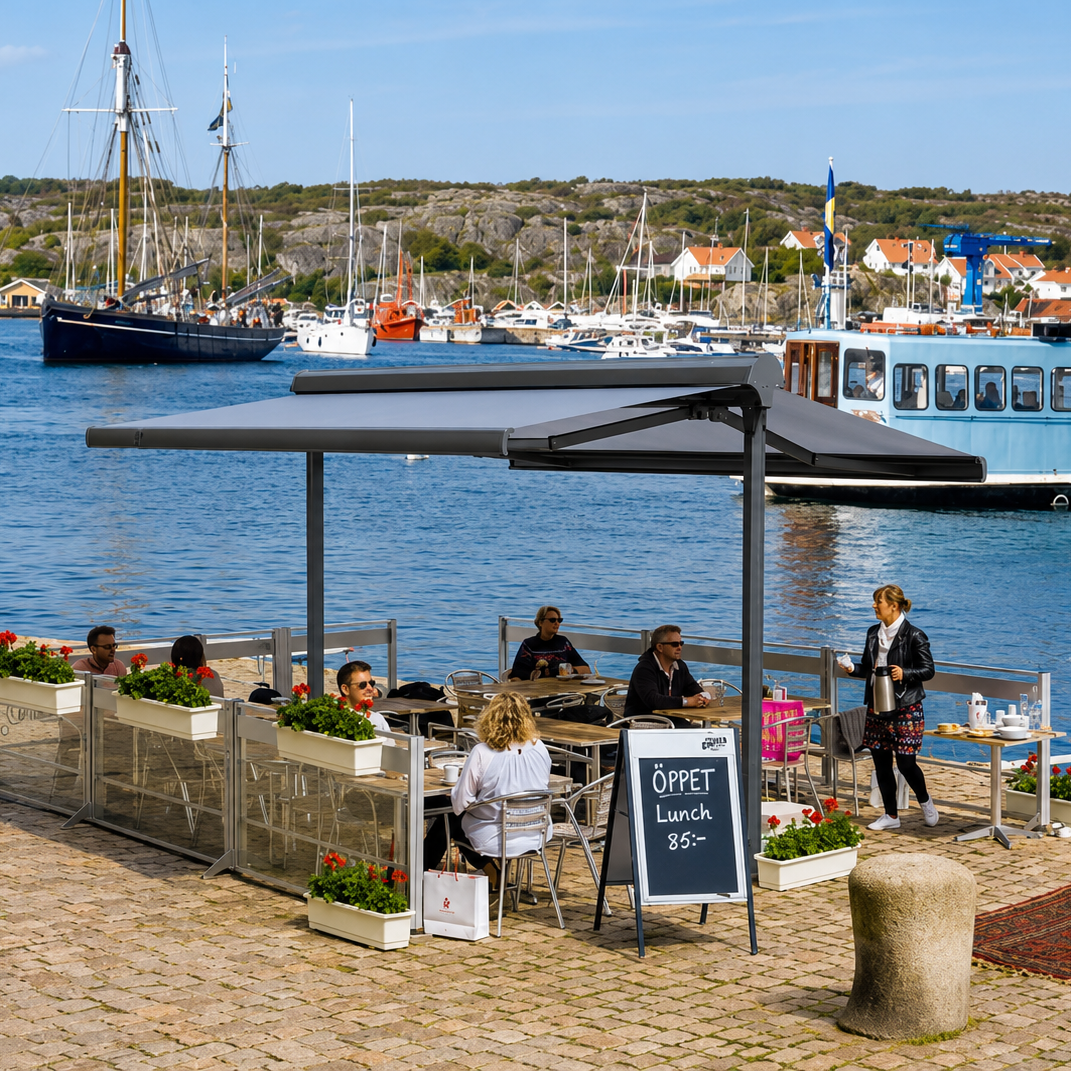 Duo markis i aluminium över uteservering vid hamn, båtar och klippkust i bakgrunden.