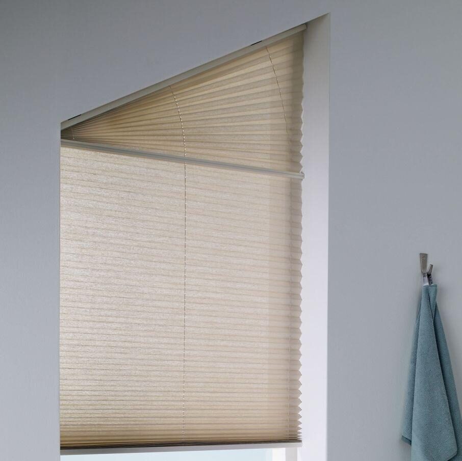 Plisségardin med specialform i beige, monterad i snedställd fönsternisch, släpper diffust ljus och skapar avskildhet