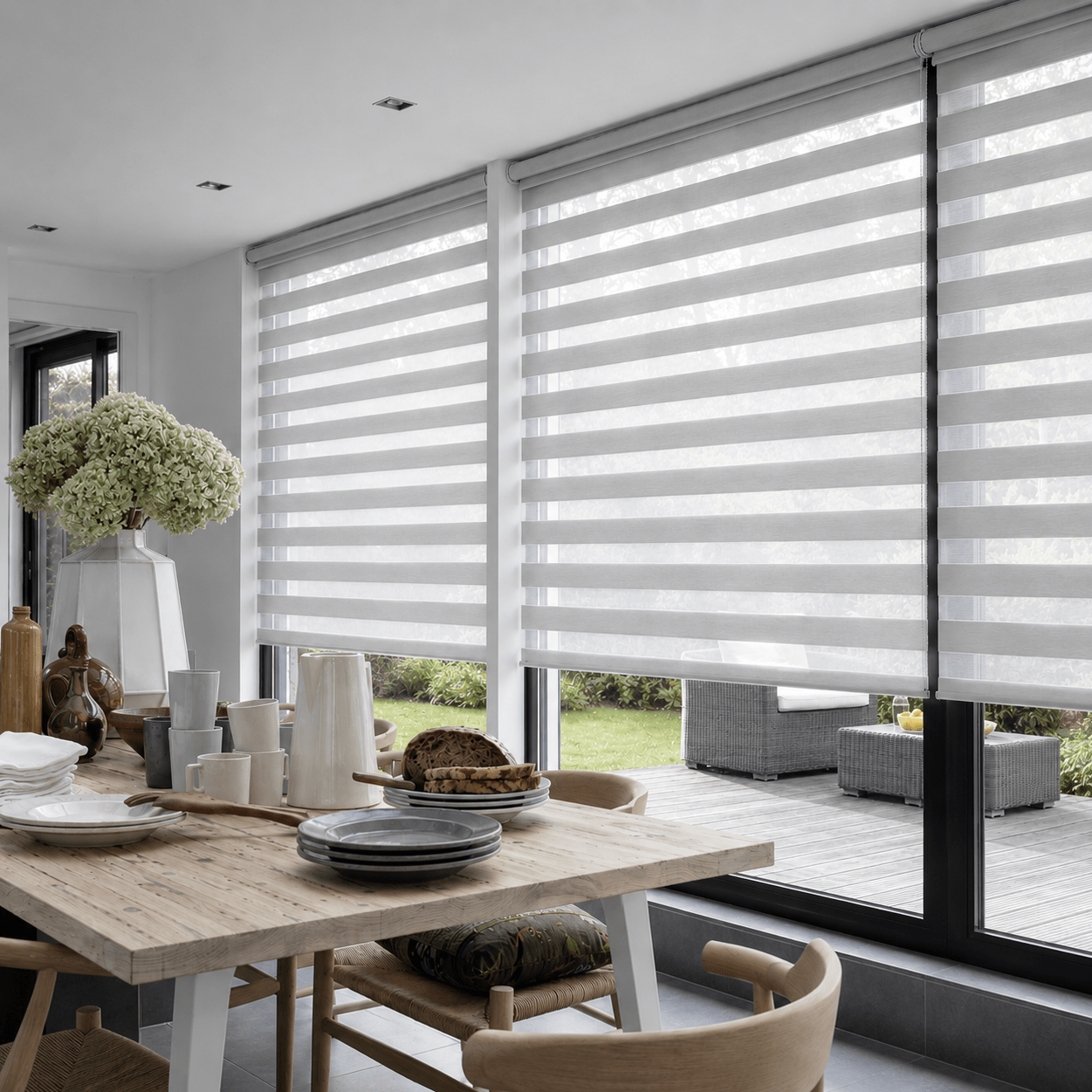Visiongardiner eller duo-rullgardiner i ljus grått på stora fönster mot uteplats i modern villa, matsalsmiljö