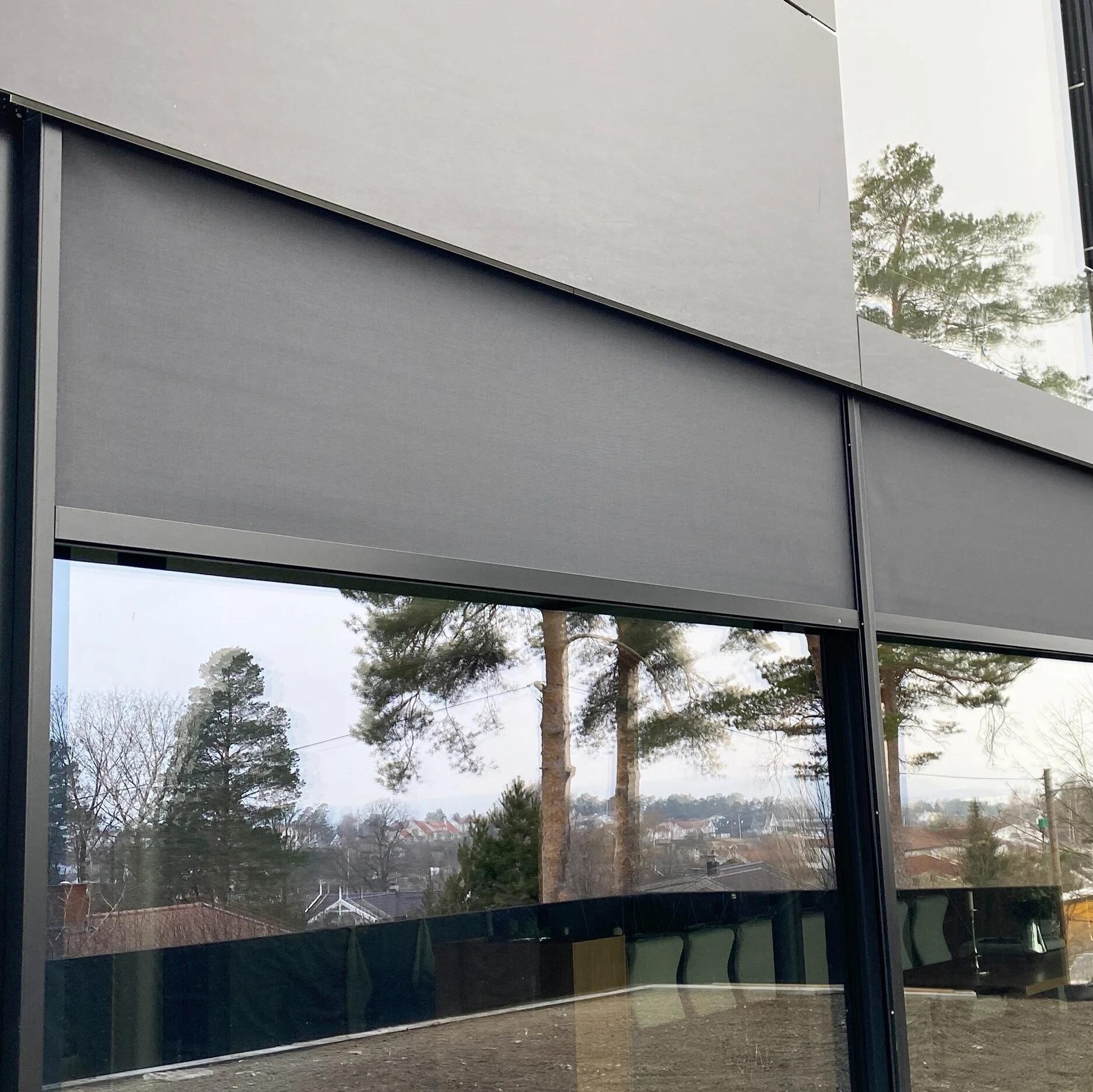 Mörka vertikalmarkiser som täcker fönster på modern villafasad, utvändigt solskydd för terrassnivå.
