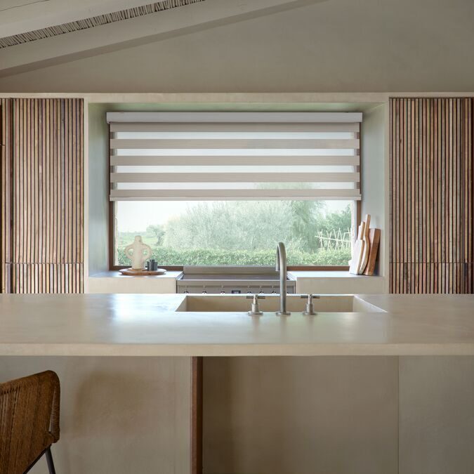 Vision/duo-rullgardin i beige monterad i köksfönster mot trädgård, modern villa med stor köksbänk och träpaneler