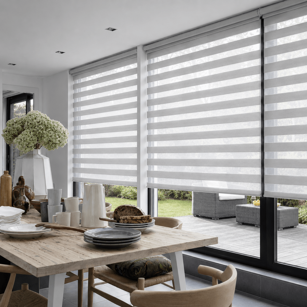 Visiongardiner eller duo-rullgardiner i ljus grått på stora fönster mot uteplats i modern villa, matsalsmiljö